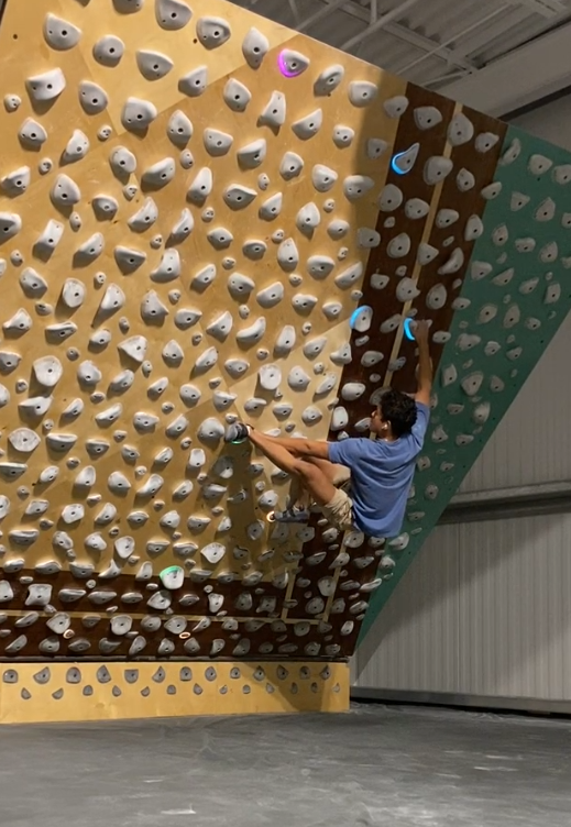 David climbing beneath an overhanging indoor training wall.